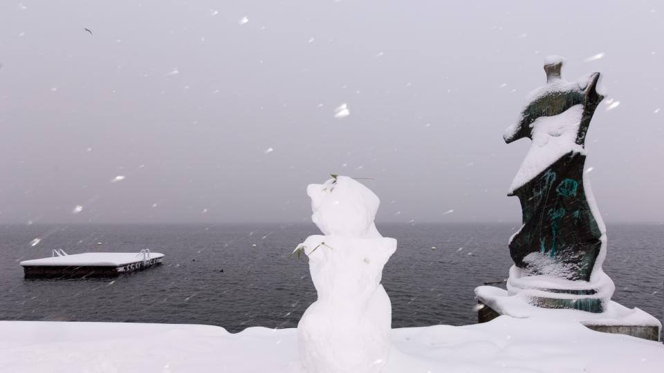 Ein Schneemann steht neben der Skulptur von Henry Moore am schneebedeckten Ufer des Zugersees.